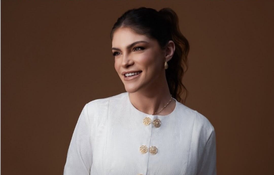 Retrato de estúdio da Dra. Bethânia Andrade, dermatologista, com fundo marrom e blazer taupe